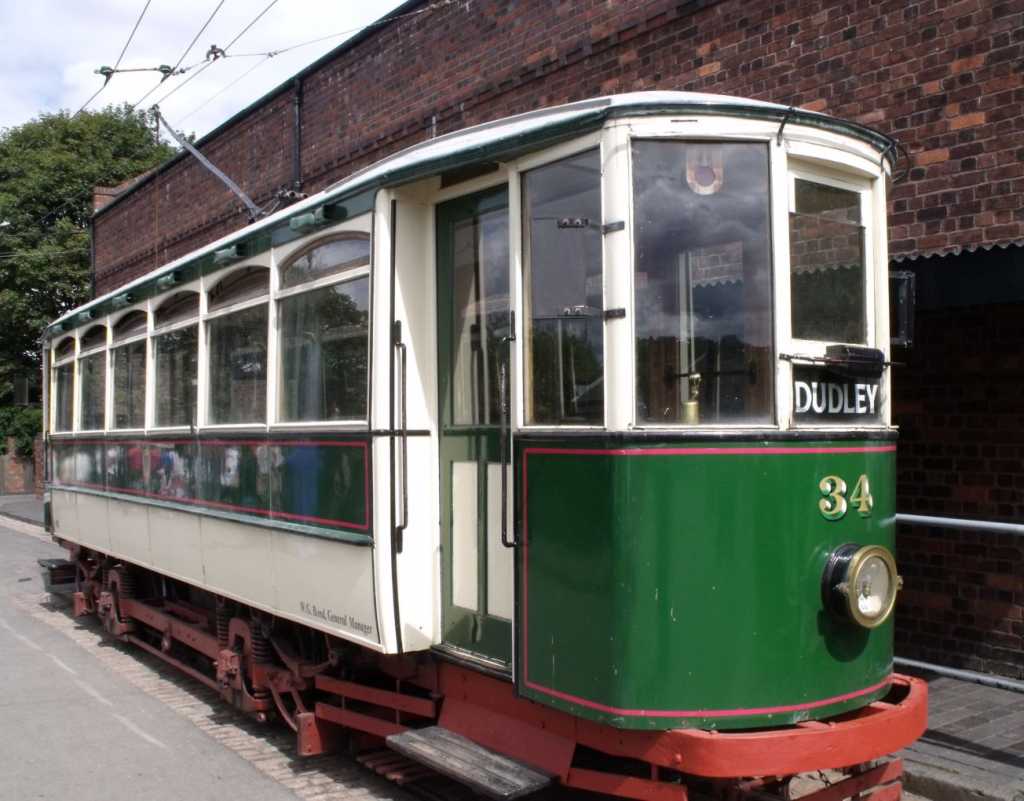 A vintage red, green and white tram with a destination sign saying Dudley mounted on the front