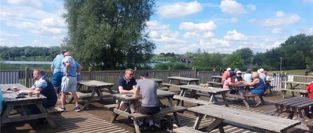 People sitting at picnic tables on decking by the water