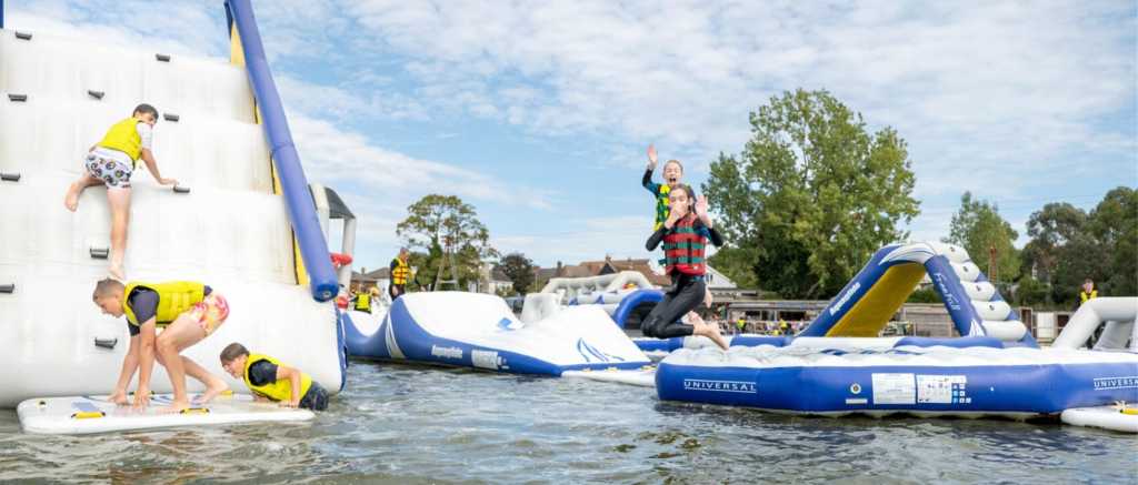 People wearing life jackets climbing and jumping their way through an inflatable obstacle course on water