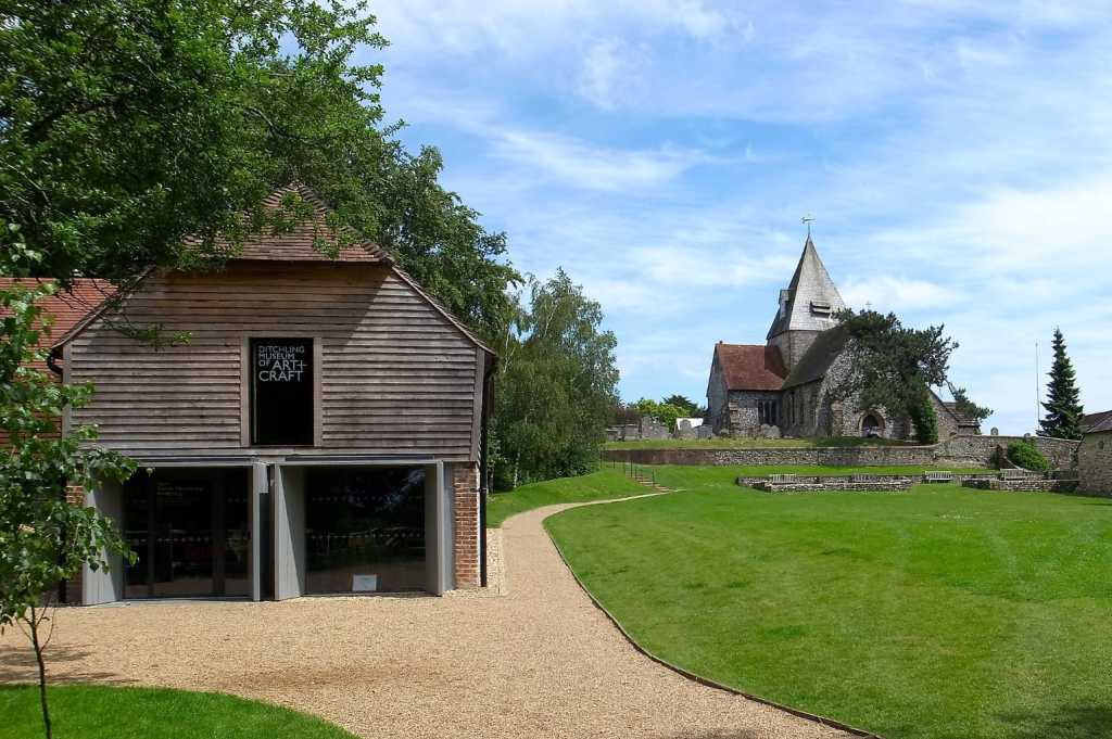 Wooden museum building with lawn in the foreground and church in the background